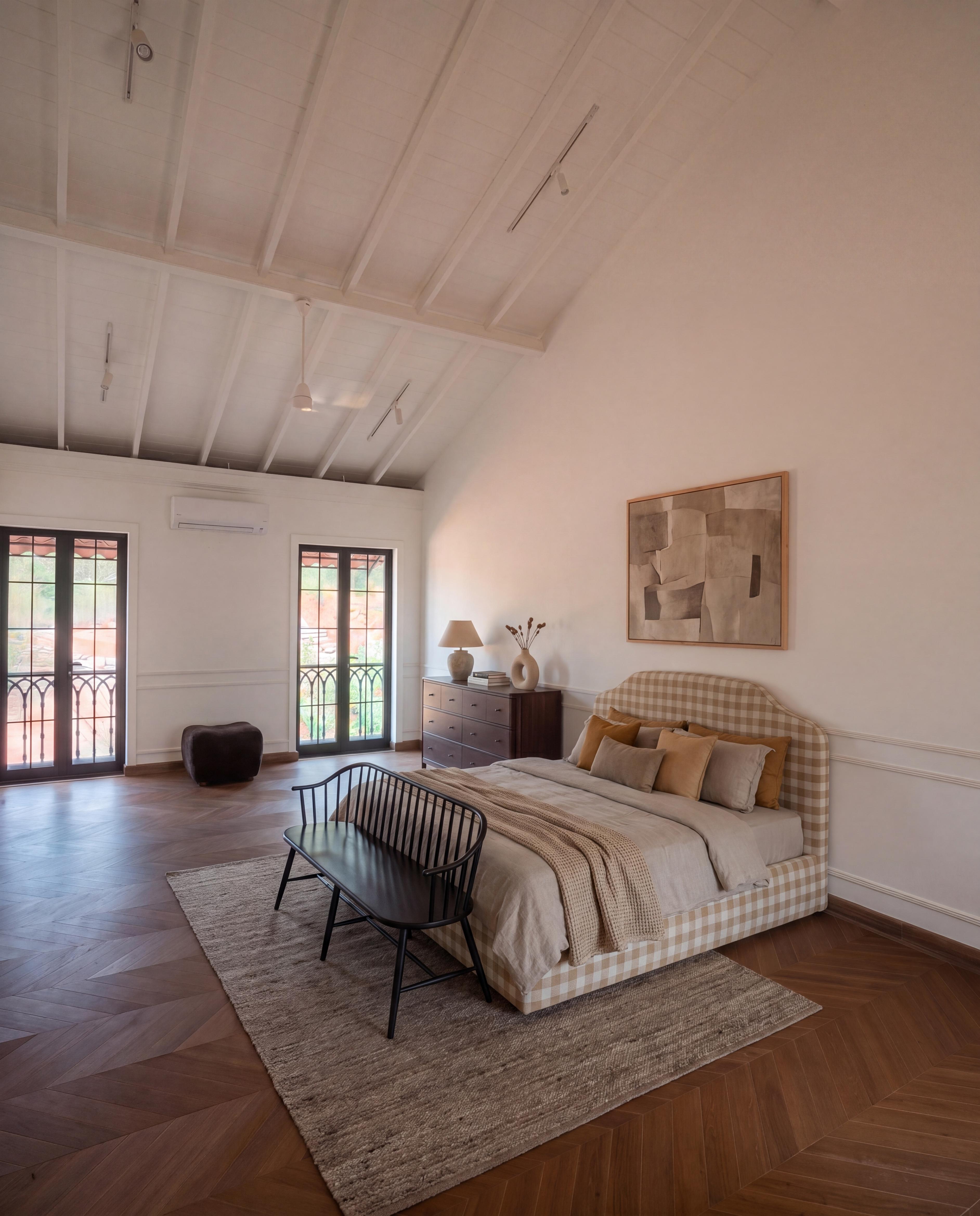 A vaulted villa bedroom, staged with a checked bed, bench, rug and artwork beneath the original timber ceiling.